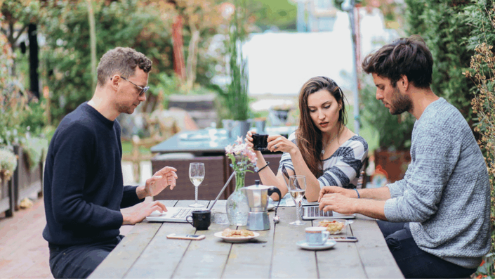 Three people enjoying coffee and networking at an outdoor Parisian café, building authentic business connections.