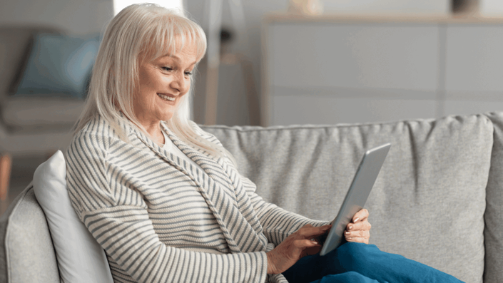 A person smiles while comfortably using a tablet on their couch, demonstrating the personalized and user-friendly mobile banking experience powered by AI and Your Bank.