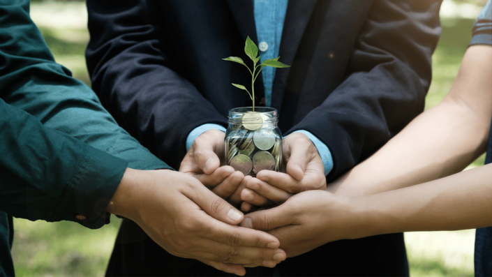 A group of people holding a jar with coins and a plant growing from it, symbolizing sustainable investing and ESG investments.